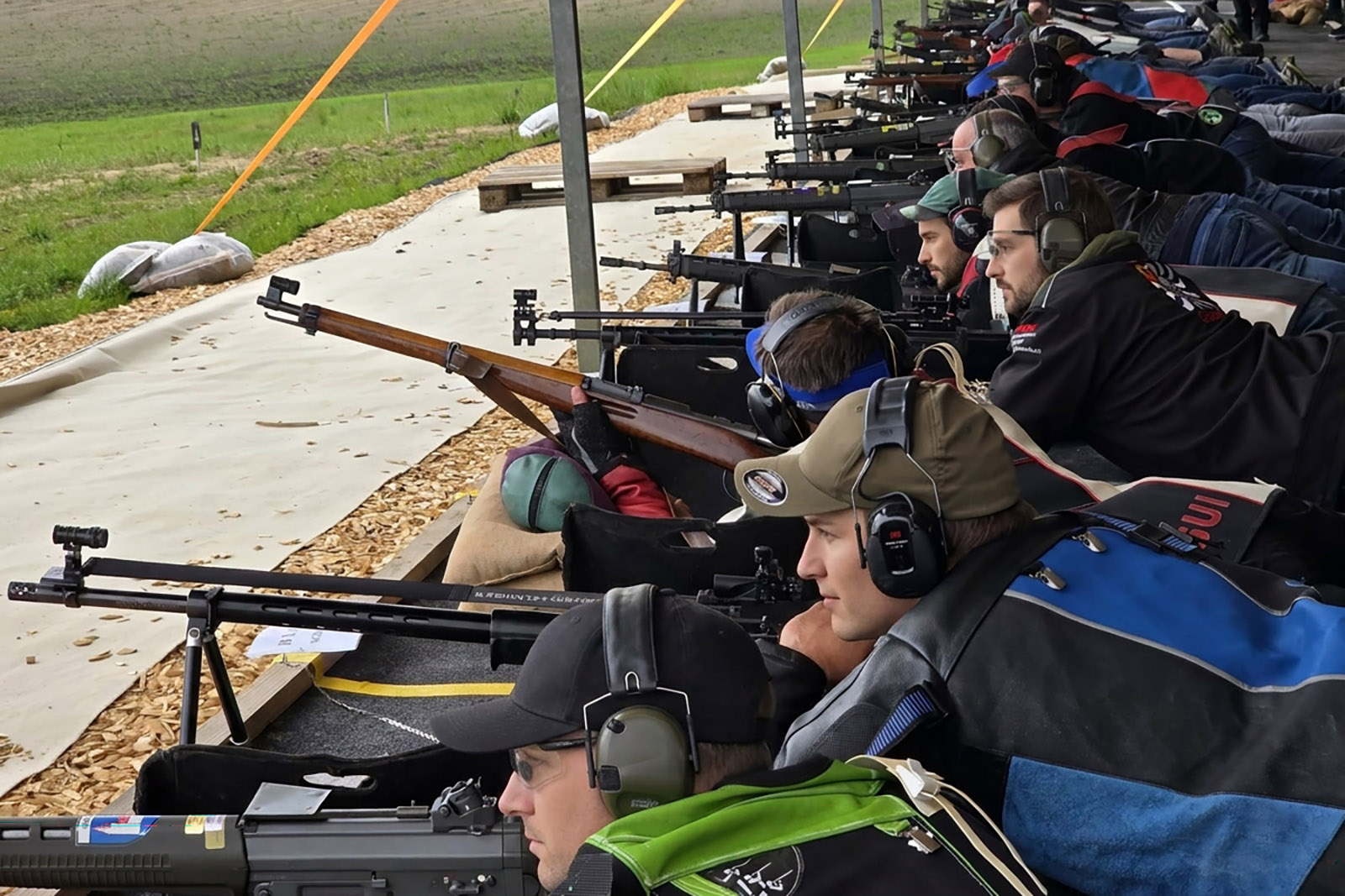Schützenlinie liegend mit Sturmgewehren, Karabinern und Standardgewehren, Heuballen und Holzschnitzel im Vordergrund