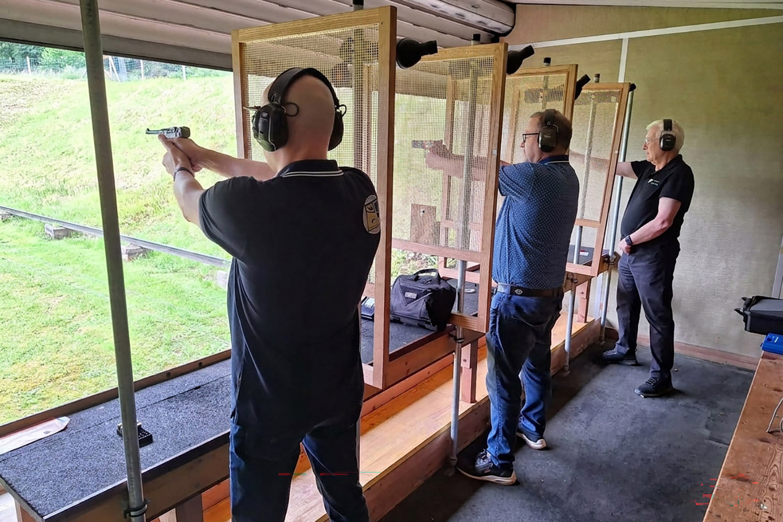 Drei Pistolenschützen mit dunkelblauen Polos im Stand, einer im Anschlag